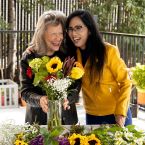 A photo of two women smiling and arranging flowers. 