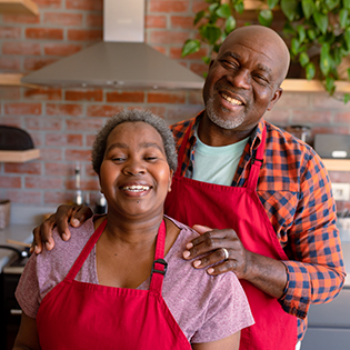 A smiling man and woman in a kitchen both wearing aprons.