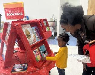 Head Start student looks at books with parent at the book fair