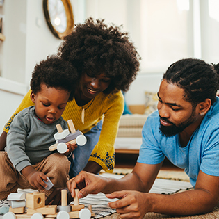 Two parents engage with child as the child builds a car out of blocks.