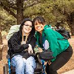 A woman posing next to a woman in a wheelchair while they both smile at the camera.