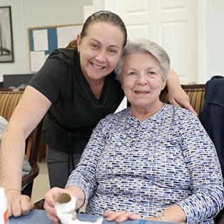 A nurse stands beside a senior who is making a craft