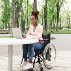 Black woman who uses a wheelchair sitting at a table using a computer.