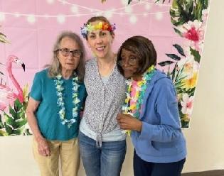 Two ADS participants and a staff member wearing leis and posing in front of a tropical backdrop.