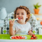 Child sitting on a high chair eating fruit 