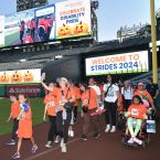 A photo of a group of people walking through the Angel Stadium wearing orange shirts with the Strides jumpotron.