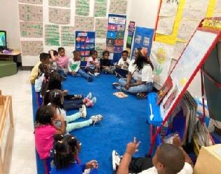 Fulton Bank employee speaking to children while seated in a circle on a classroom rug.