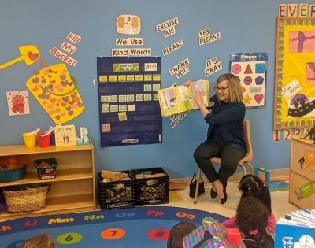 Volunteer reading a book to students in a classroom.