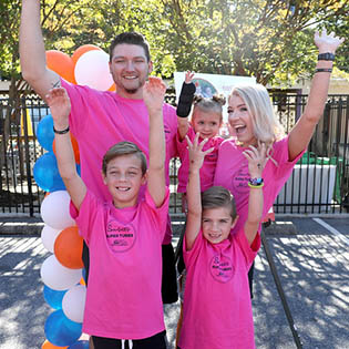 Family with five people all cheering with pink shirts on and smiling