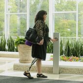 a woman with a prosthesis for her right leg swipes a key card to access an office building. She is wearing a dress and carrying a tote bag.