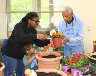 Easterseals staff member assists and a senior and a child with potting flowers.
