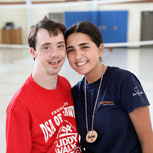 adult with disability standing with camp counselor in gymnasium at camp