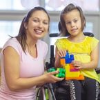 a therapist holds a toy with a young girl in a wheelchair