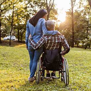 A caregiver standing next to a person in a wheel chair as they face the sunset.