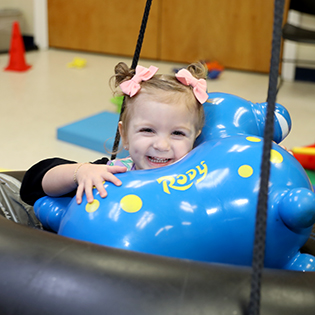 child with bows in her hair on physical therapy tube swing holding a blue toy