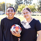 Smiling man and woman posing with soccer ball.