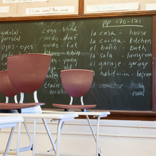 Classroom with chalkboard. Written on the chalkboard is a list of words in English, accompanied by their Spanish translations.