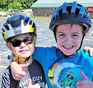 photo of two boys in bike helmets hugging and giving the thumbs up sign