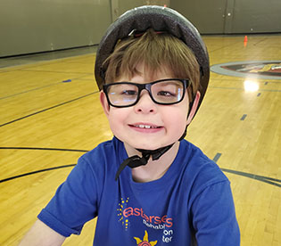 photo of a brown haired boy wearing a bike helmet and glasses with a purple t-shirt on