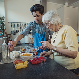 a young man helping a senior woman cook in a kitchen.
