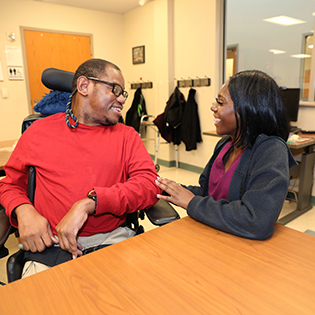 Direct support professional talking to an adult with a disability in wheel chair